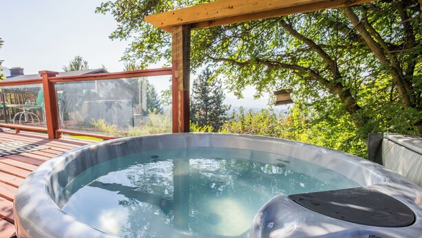 Ein Whirlpool auf einer Holzterrasse mit einer Pergola darüber, umgeben von Grünpflanzen.