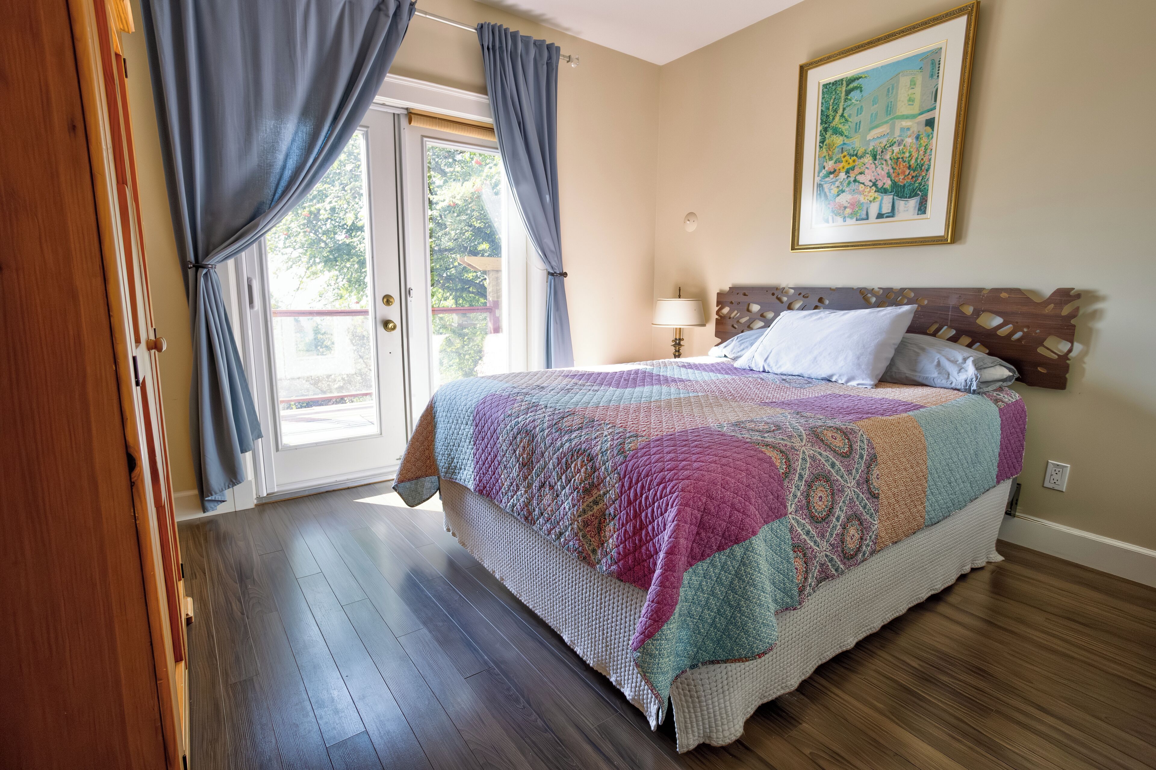 Ein Schlafzimmer mit einem großen Bett, einem Holzkopfstück, einer Tür mit Vorhängen und einem Gemälde an der Wand.