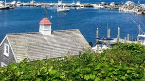 A marina with boats docked, a building with a red roof, and greenery in the foreground. - Magical House in the Trees with Water View - Secluded Area (Aquinnah)