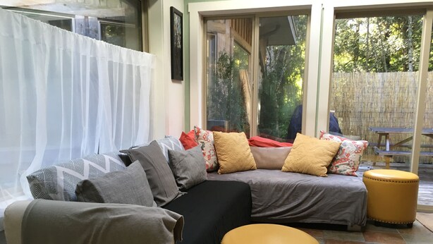 A cozy living area with a sectional sofa, a small round ottoman, and a window with sheer curtains. - Chesterman Beach Fine Art Vacation House - Walking distance to North Chesterman (Tofino)