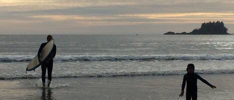 A beach scene with two people, one holding a surfboard and the other walking with a toy.