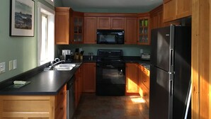 A kitchen with wooden cabinets, a black refrigerator, a microwave, and a stove. - Chesterman Beach Fine Art Vacation House - Walking distance to North Chesterman (Tofino)