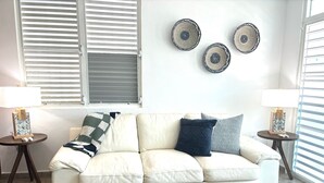 Un salon avec un canapé blanc, deux tables d’appoint avec des lampes, une table basse et des assiettes décoratives accrochées au mur.