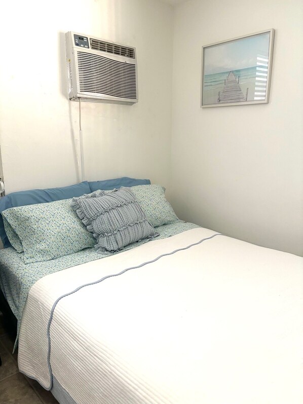 A bedroom with a bed, a wall-mounted air conditioner, and a framed picture on the wall.
