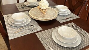 Une table à manger dressée avec de l’assiette, des bols et des couverts blancs, le tout posé sur des sets de table à rayures.