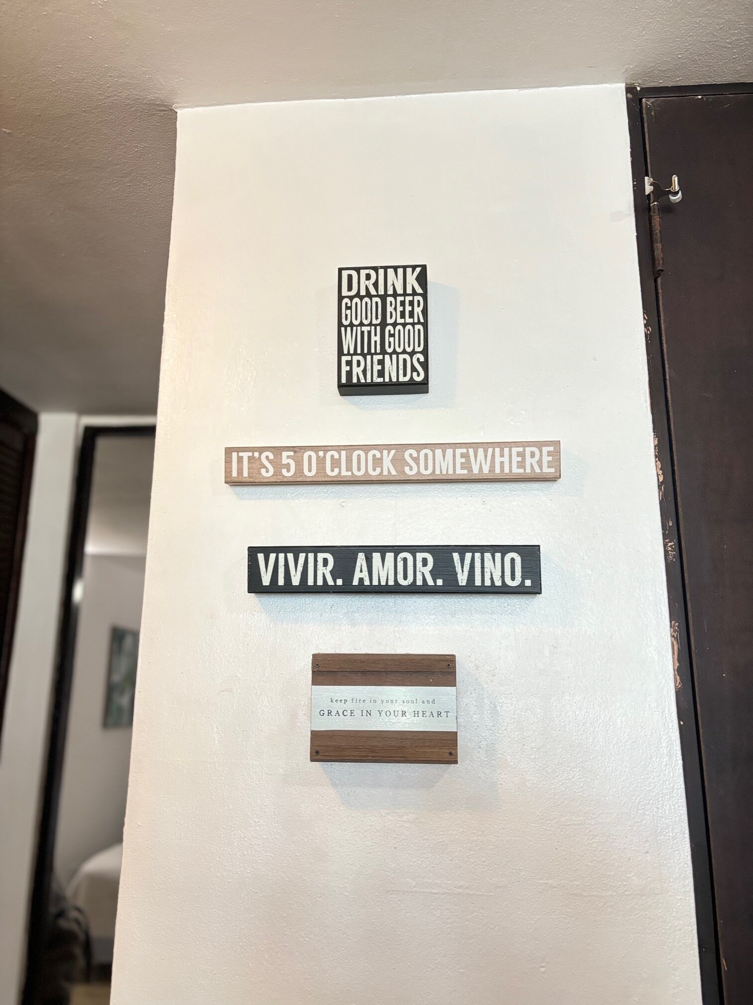 Een muur met inspirerende bordjes, waaronder ‘Drink goed bier met goede vrienden’, ‘Het is ergens 5 uur’ en ‘Vivir. Amor. Vino.’