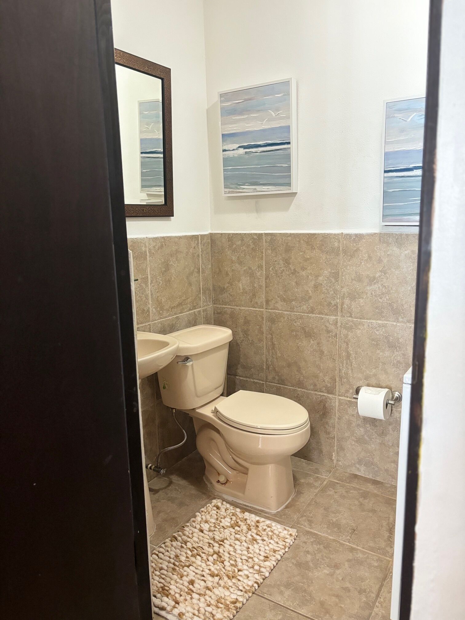 A bathroom with a toilet, sink, and two framed pictures on the wall.
