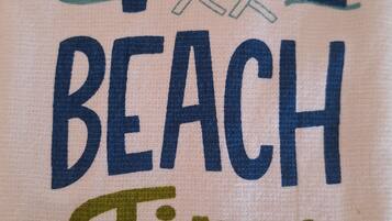 En handduk med texten ”NU ÄR DET STRANDTID” och en illustration av ett strandparasoll och en strandstol.
