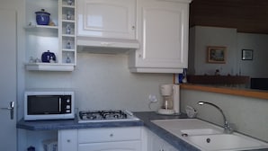 Une cuisine compacte avec des meubles blancs, un four à micro-ondes, une cuisinière à gaz, une machine à café et un évier.