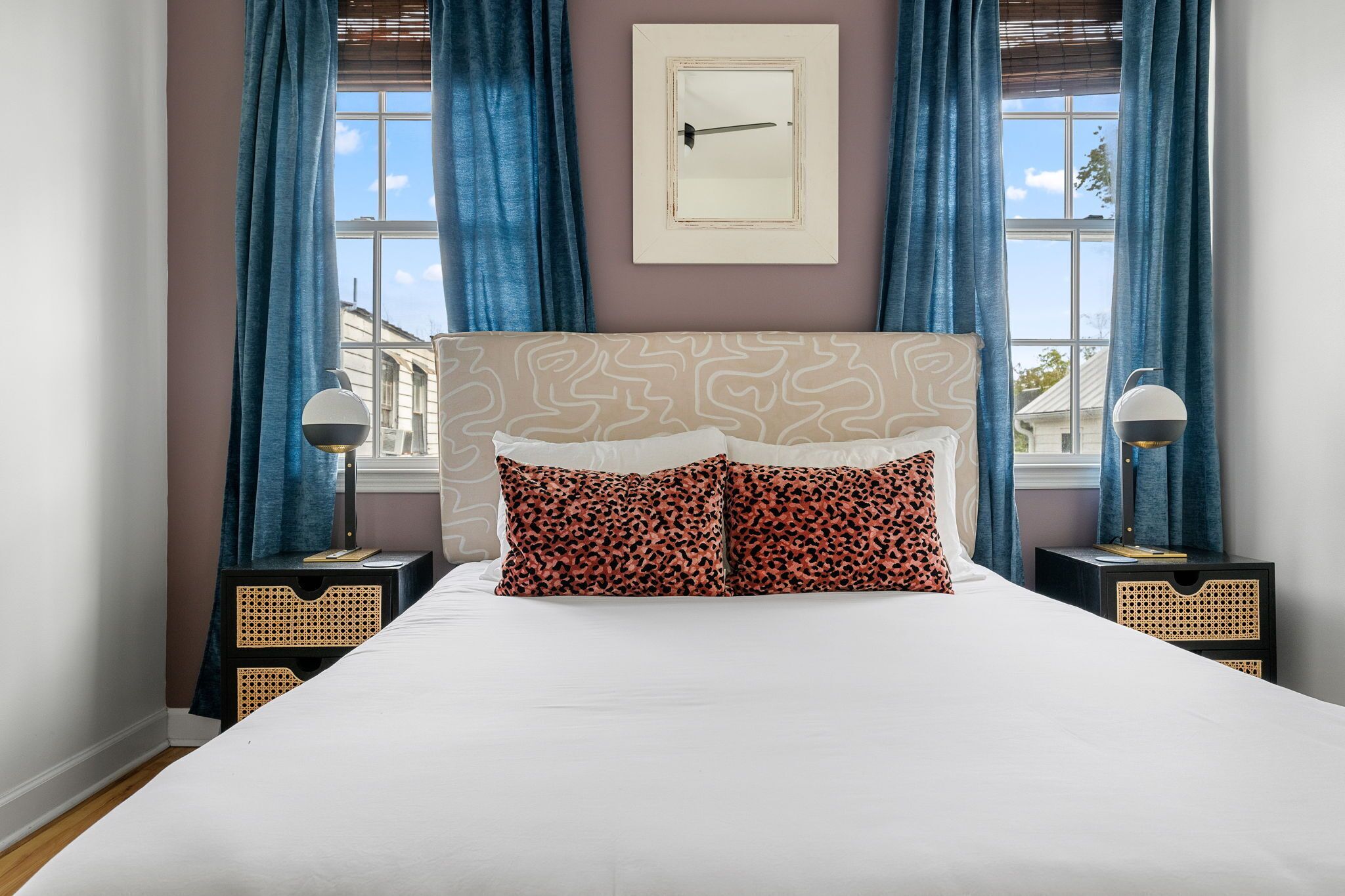 A bedroom with a large bed, two nightstands, a wall-mounted picture, and a window with curtains.