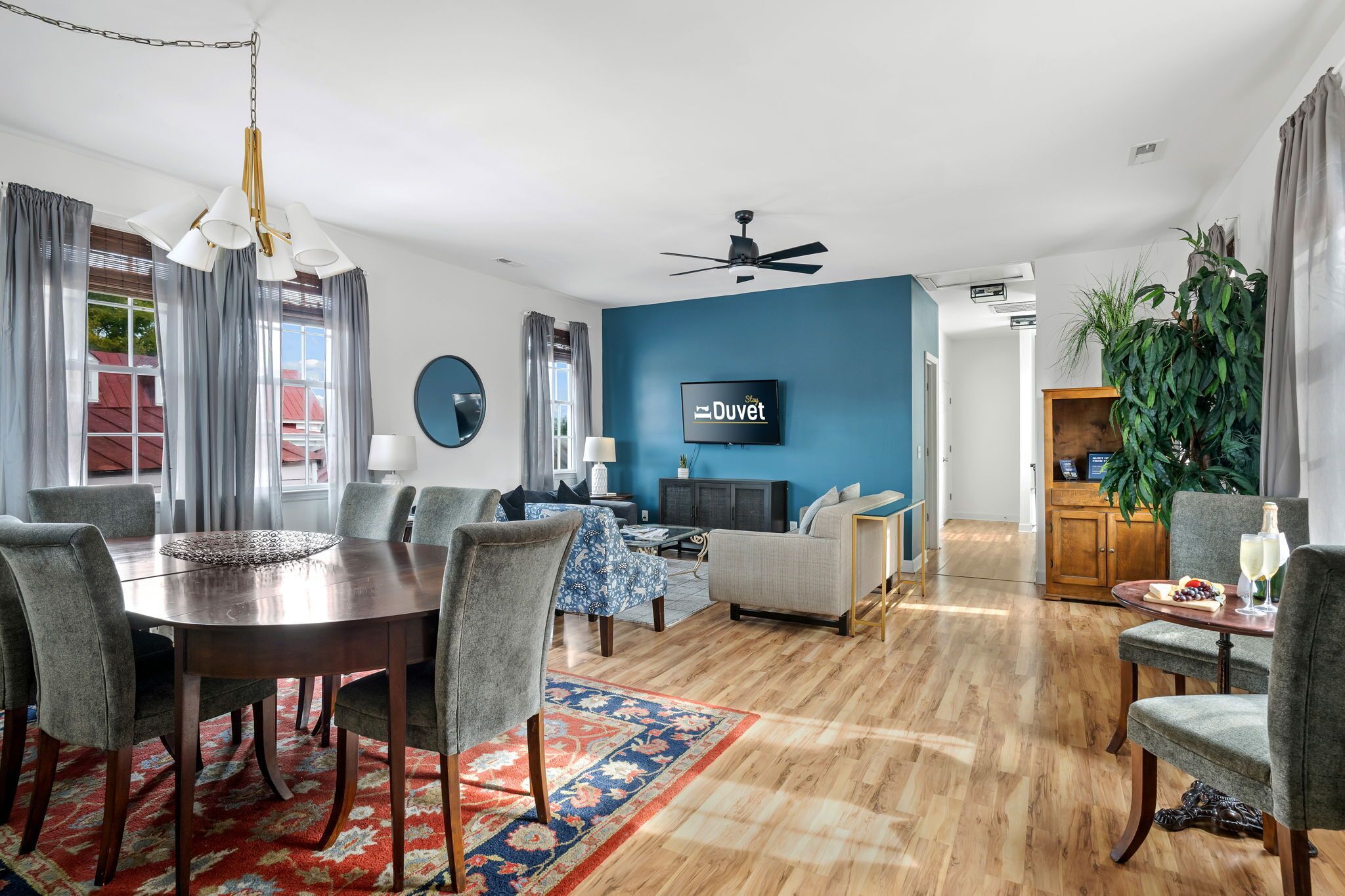 A modern living room with a blue accent wall, a dining area with a round table, and a TV mounted on the wall.