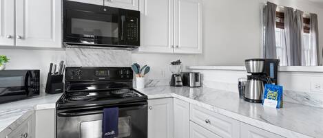 A modern kitchen with white cabinetry, a black stove, a microwave, and a coffee maker.