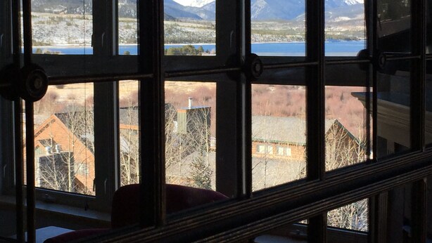 A room with large windows offering a view of a snowy mountain range and a lake. - On Lake Dillon with Amazing Views Everywhere! Hot Tub, Grill, Private Balcony! (Frisco)