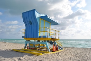 A lifeguard tower at Miami Beach with a blue and yellow color scheme, located on a sandy beach with the ocean in the background.