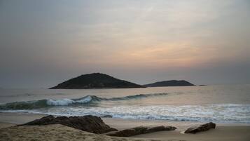 A beach with waves, rocky outcrops, and distant islands under a cloudy sky.