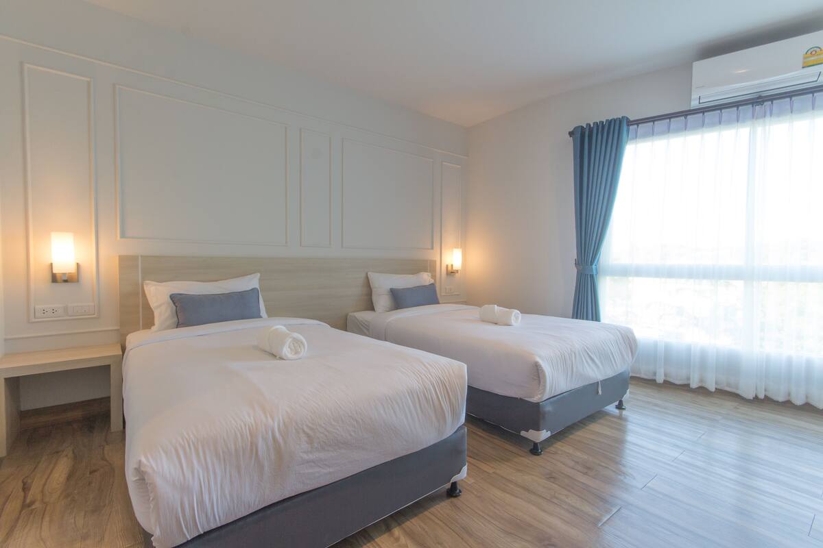 A hotel room with two beds, a bench, and a window with curtains.