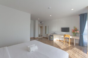 A hotel room with a bed, a desk, a chair, a television, and a small trash bin. - Donchan Grand Hotel (Chiang Mai)