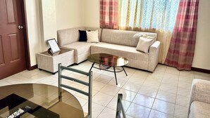 A living room with a sofa, a glass coffee table, a side table, a chair, and a door. - Cranberry's Place (Iloilo)