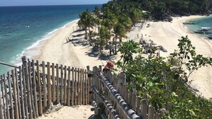 A beach with a wooden fence, palm trees, and boats in the water. - Cranberry's Place (Iloilo)