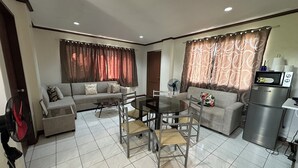 A living room with a sofa, a dining table with chairs, a refrigerator, and a fan. - Cranberry's Place (Iloilo)