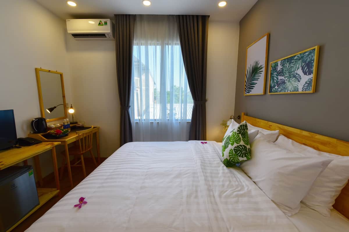 A hotel room with a bed, a desk with a computer, a chair, an air conditioner, and a window with curtains.