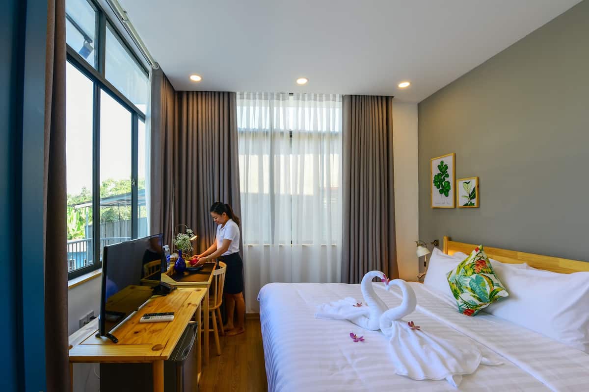A hotel room with a bed, a desk, a chair, and a window with curtains.