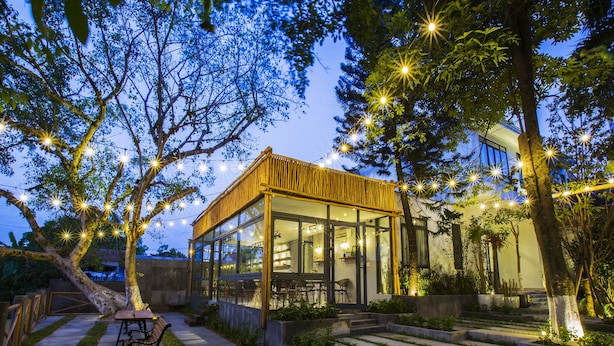 Una casa moderna con fachada de vidrio, rodeada de árboles y mobiliario exterior.