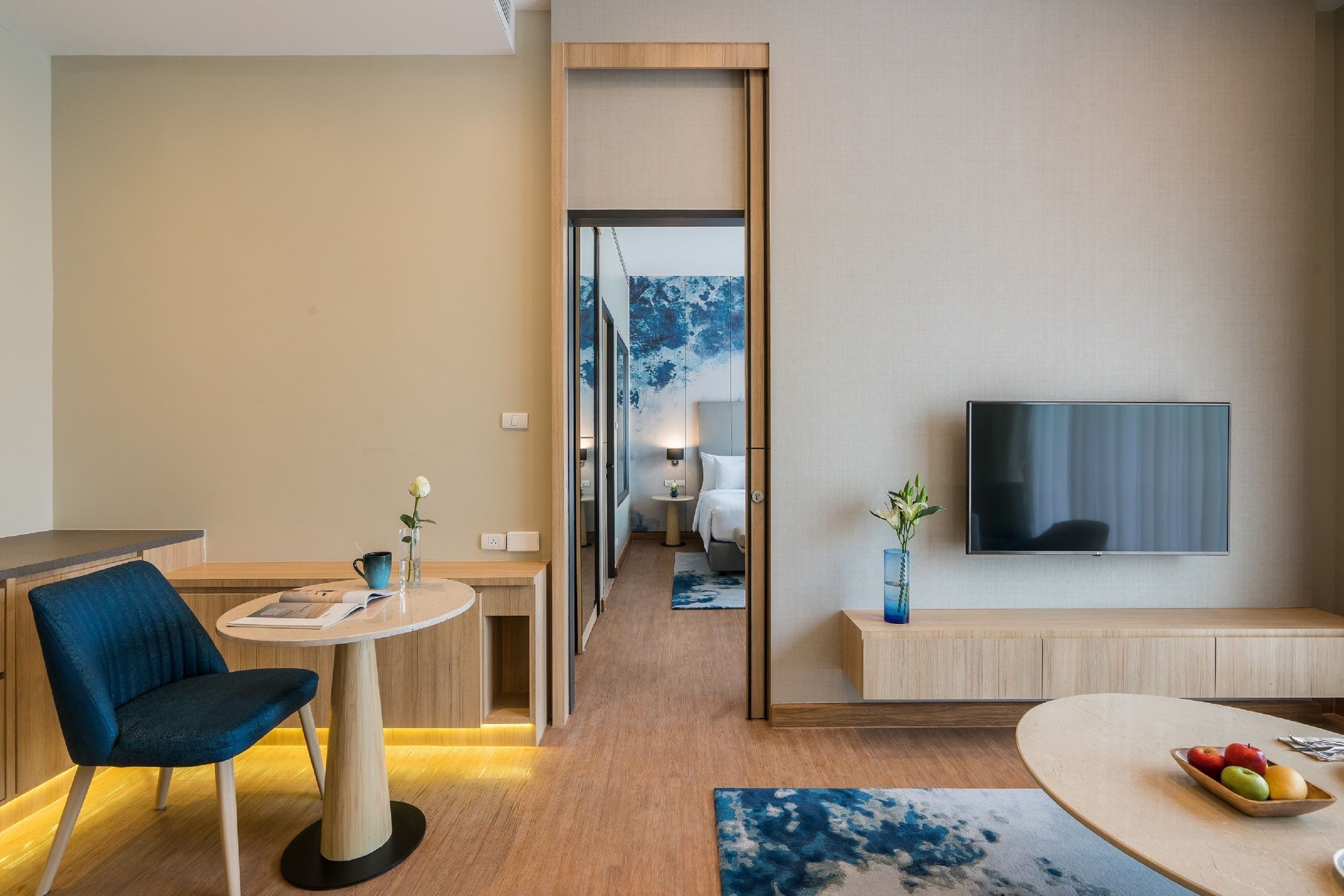 Habitación de hotel moderna con comedor, televisor montado en la pared y vista al dormitorio.