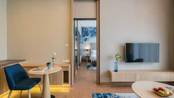 Habitación de hotel moderna con comedor, televisor montado en la pared y vista al dormitorio.