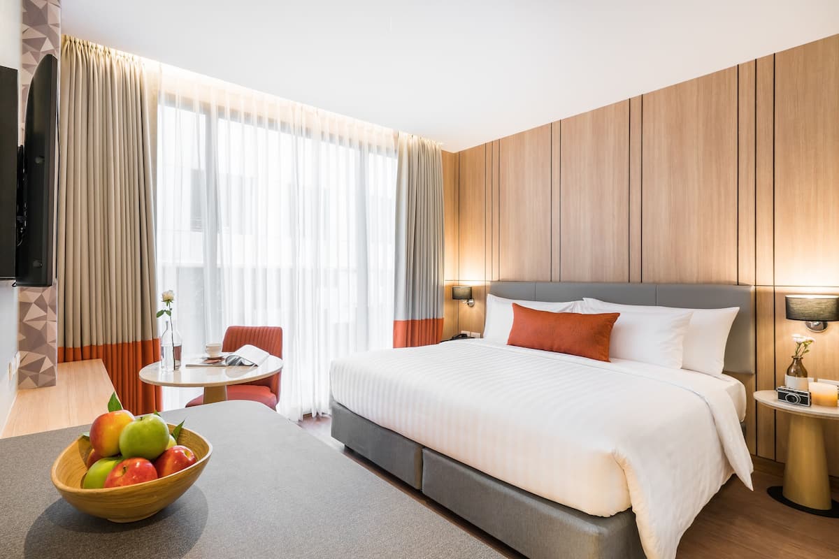A hotel room with a large bed, a dining table, a bowl of fruit, and a TV.