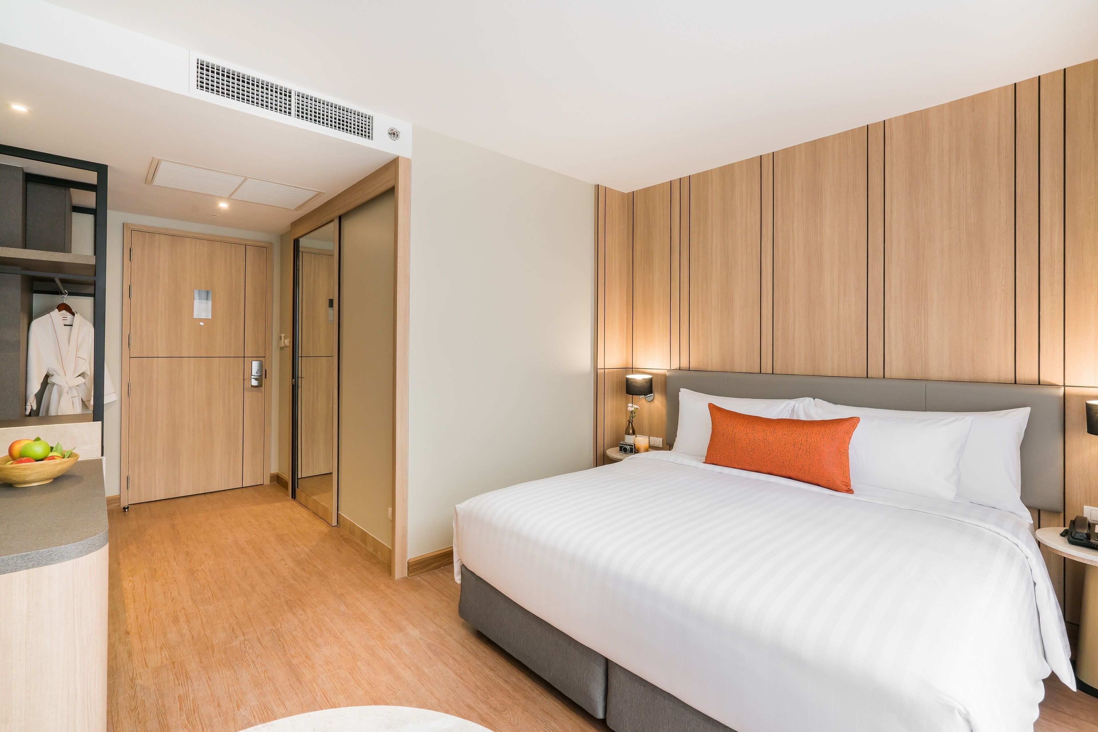 Une chambre d’hôtel moderne avec un grand lit, des murs lambrissés, une table de chevet avec une lampe et une armoire.