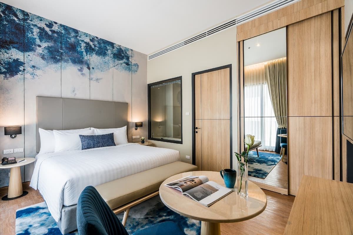 A modern hotel room with a large bed, bedside tables, a round coffee table, and a large mirror.