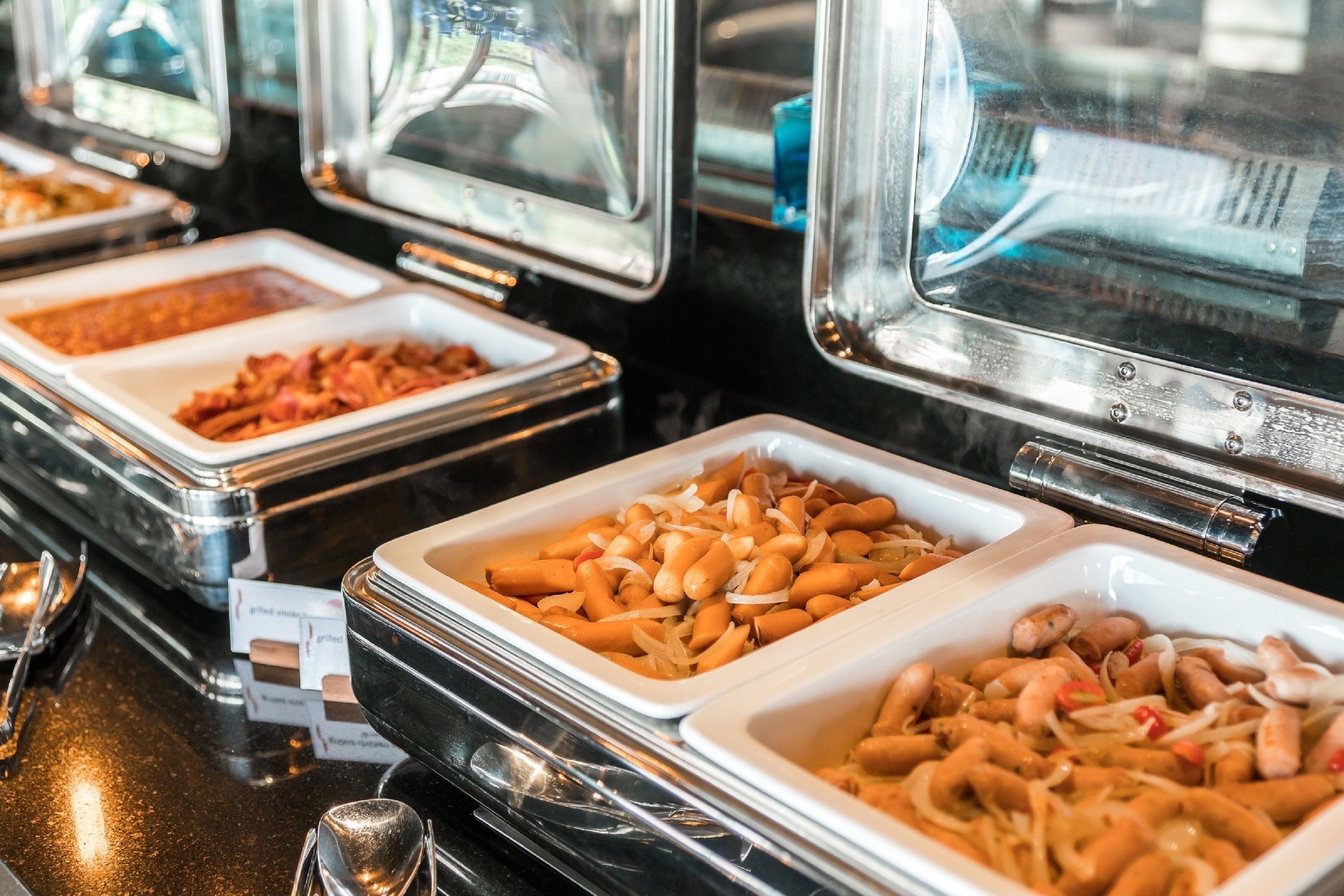 Un buffet proposant divers plats présentés dans des plateaux, notamment des saucisses et d’autres mets.