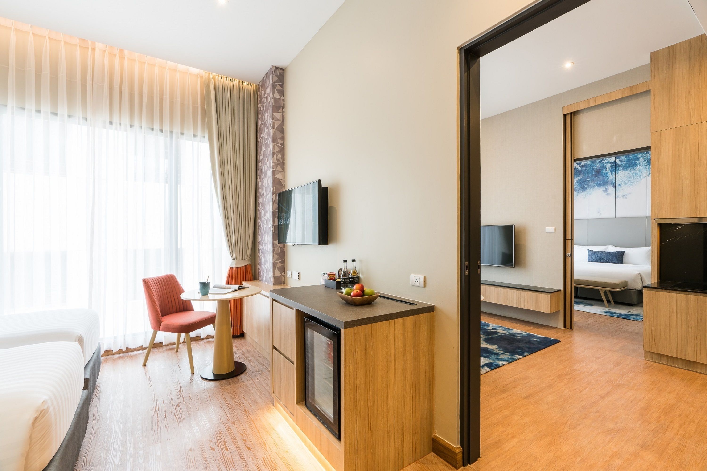 A modern hotel room with a wooden desk, a bed, a TV, and a dining area with a chair and table.