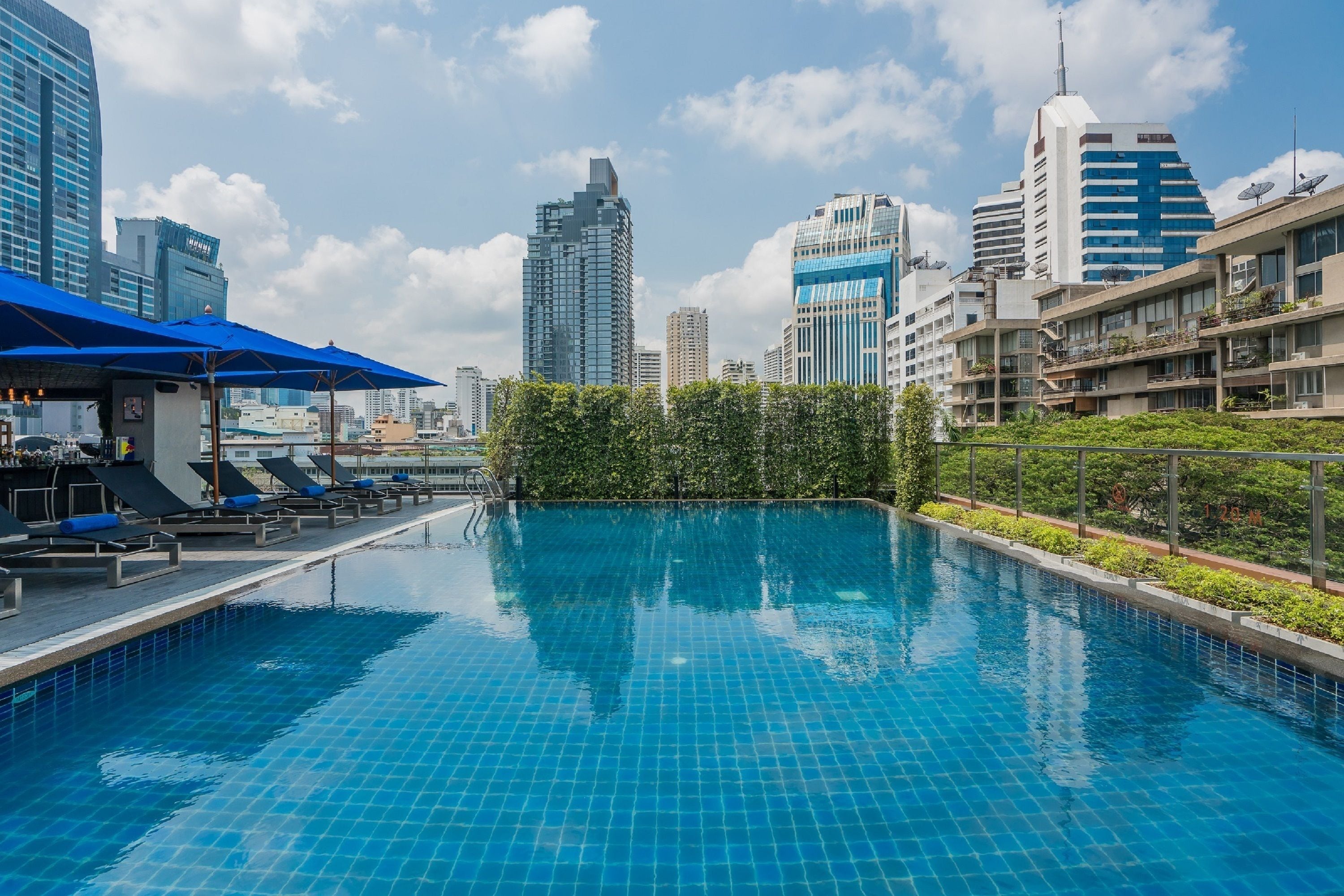 A swimming pool with lounge chairs and umbrellas, surrounded by high-rise buildings and greenery.