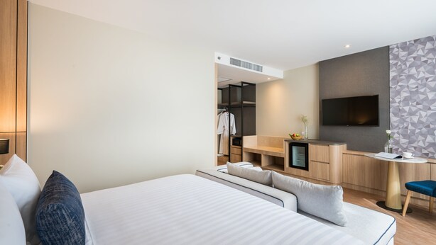 A modern hotel room with a large bed, a desk, a TV, and a kitchenette.