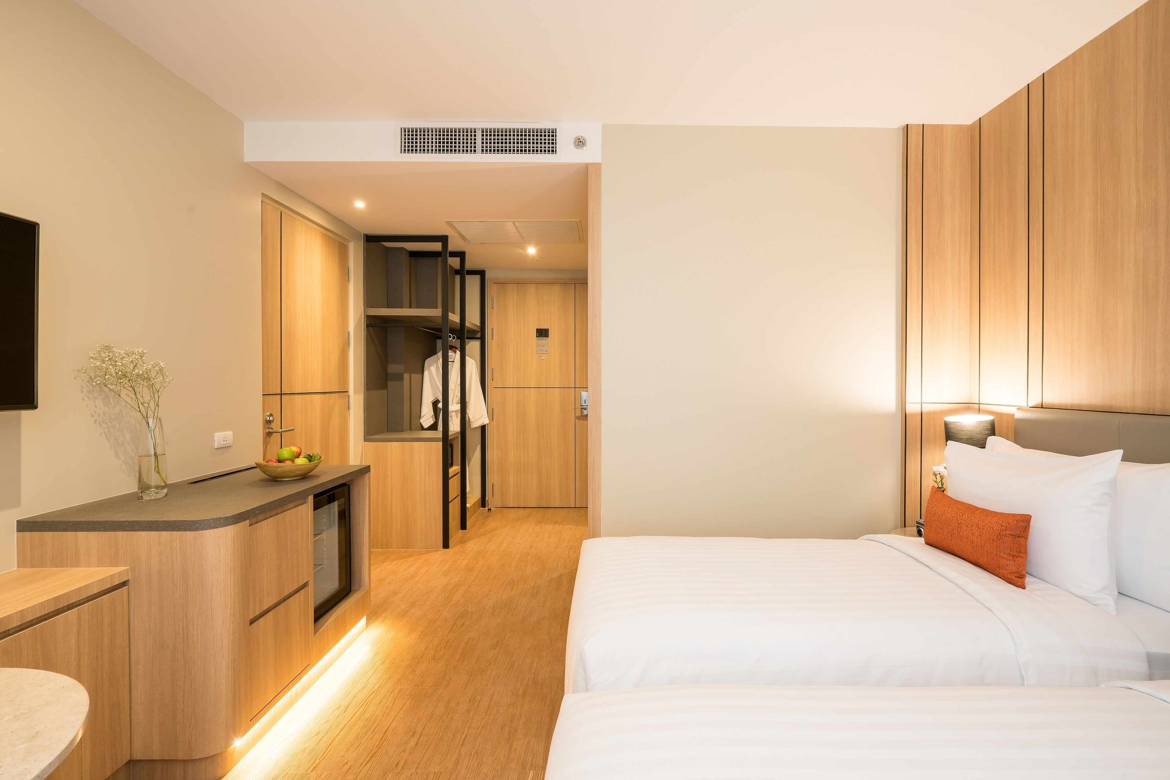 A modern hotel room with a bed, bedside table, and a small kitchenette area.
