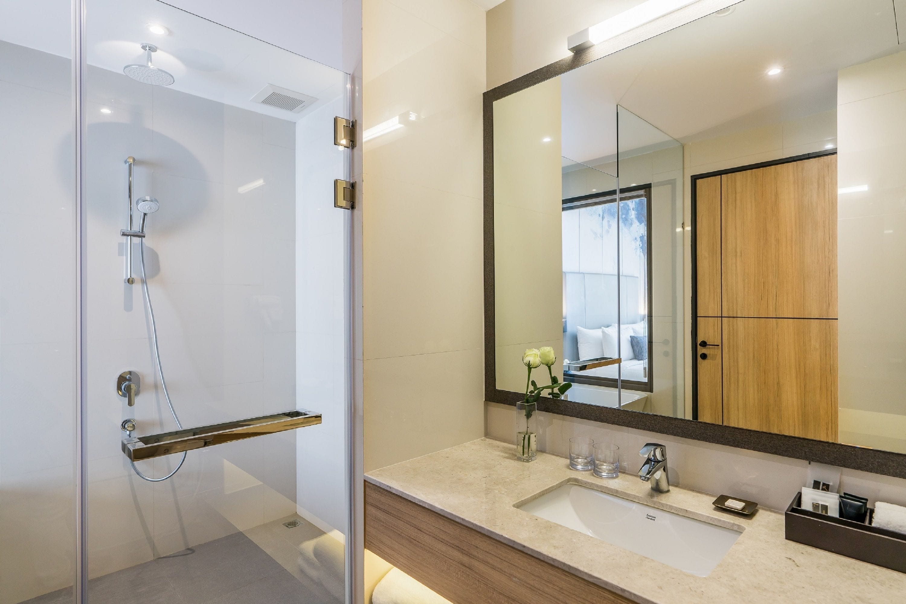 A modern bathroom with a glass shower enclosure, a large mirror, and a vanity with a sink and countertop.