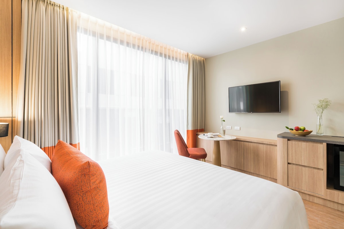 A hotel room with a large bed, a desk, a chair, and a TV mounted on the wall.