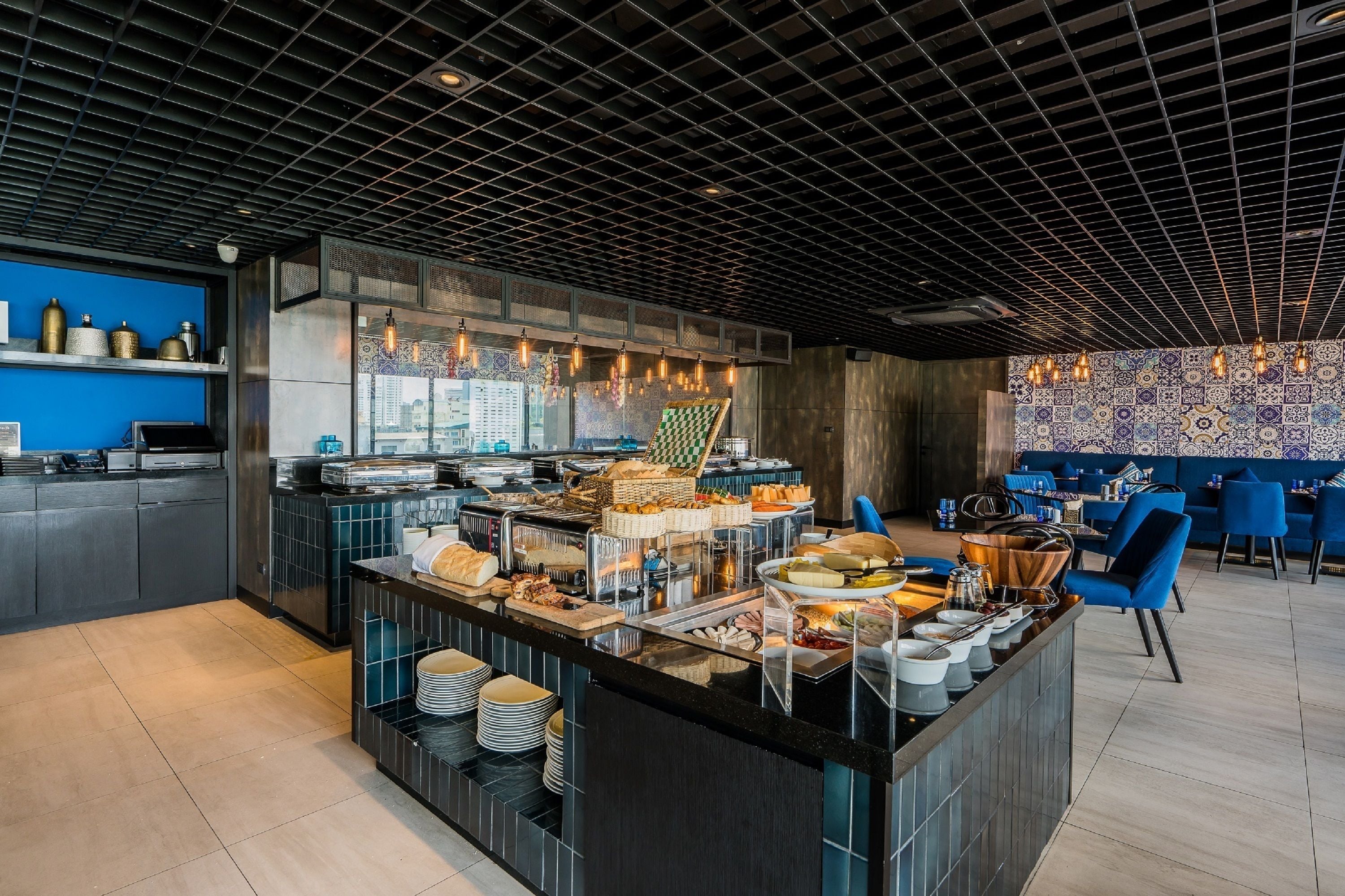 A modern restaurant with a buffet setup, blue chairs, and a patterned wall.