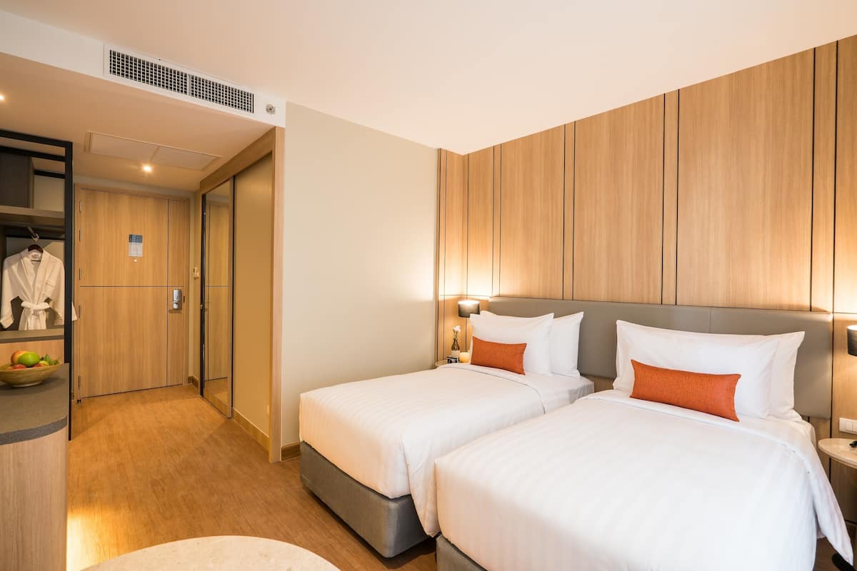 A hotel room with two beds, a wardrobe, and a small seating area.