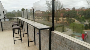 A balcony with a tiled floor, a glass partition, and a metal table with chairs. - Dalat Sky Hostel (Xuan Huong - Da Lat)