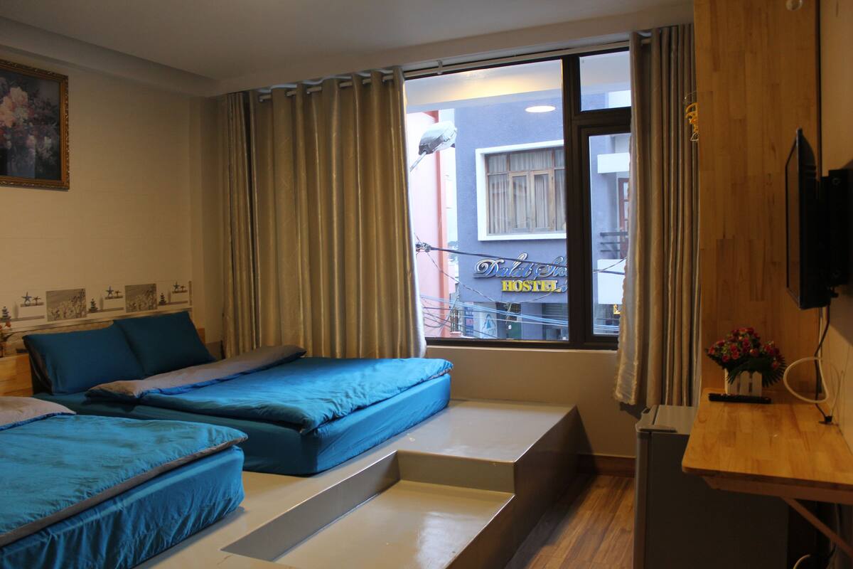 Habitación de hotel con dos camas, un escritorio de madera, televisor y ventana con cortinas.