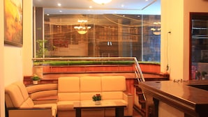 A modern living room with a sofa, a coffee table with a flower, and a large window with a view of a building and greenery. - Dalat Sky Hostel (Xuan Huong - Da Lat)