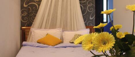 A bed with a canopy, a yellow pillow, and a vase with yellow flowers.
