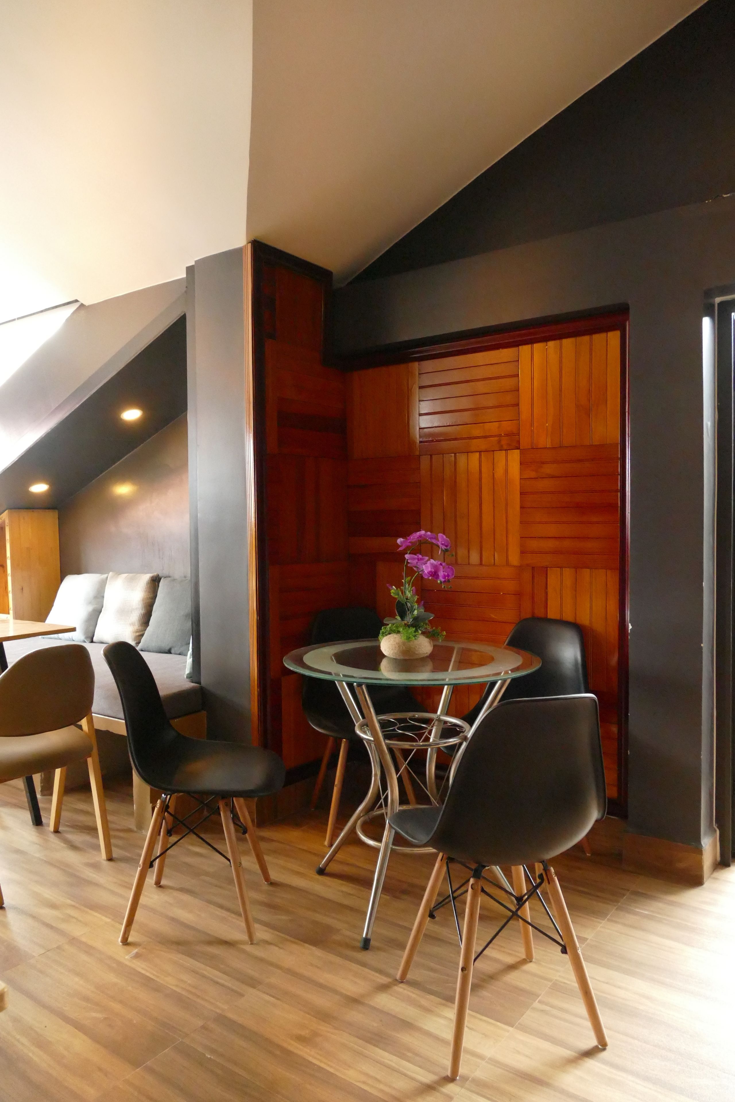 A dining area with a round glass table, black chairs, and a wooden accent wall.