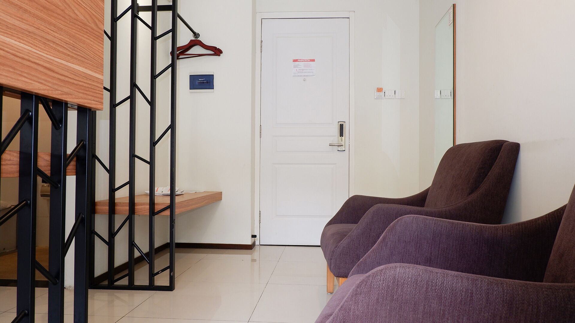 A hotel room with a staircase, a door with a notice, and two purple chairs.