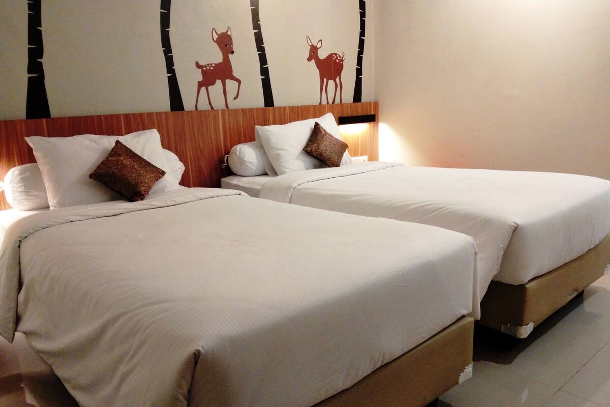 Ett hotellrum med två sängar, båda med vita sängkläder och bruna kuddar. Ovanför sängarna finns en väggdekoration i form av silhuetter av rådjur.