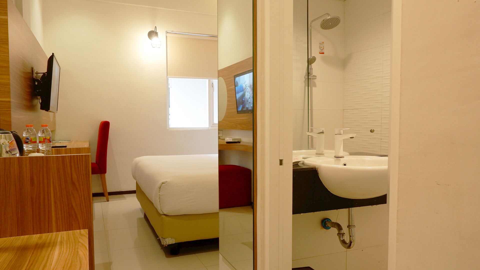 Ein Hotelzimmer mit Bett, Fernseher, Schreibtisch mit Stuhl sowie einem Badezimmer mit Waschbecken und Dusche.