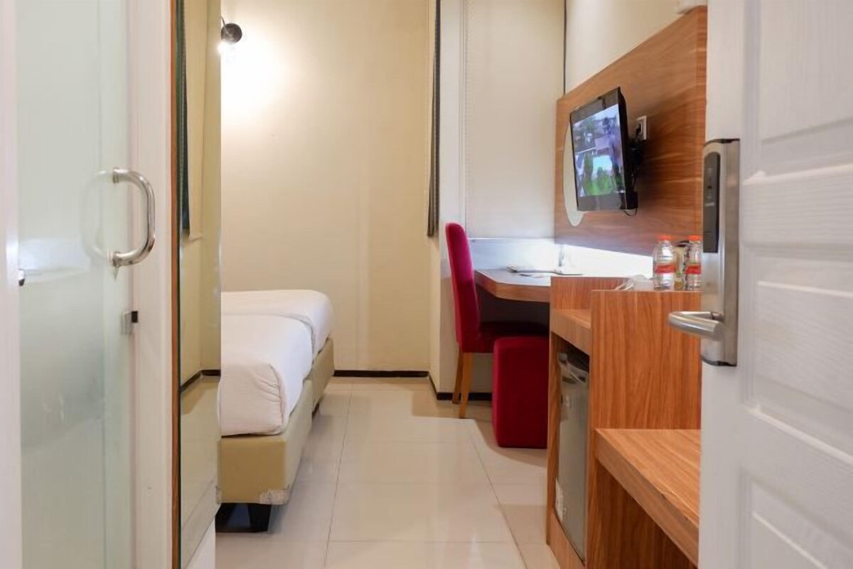 A compact hotel room with a bed, a small desk, a chair, and a TV mounted on the wall.